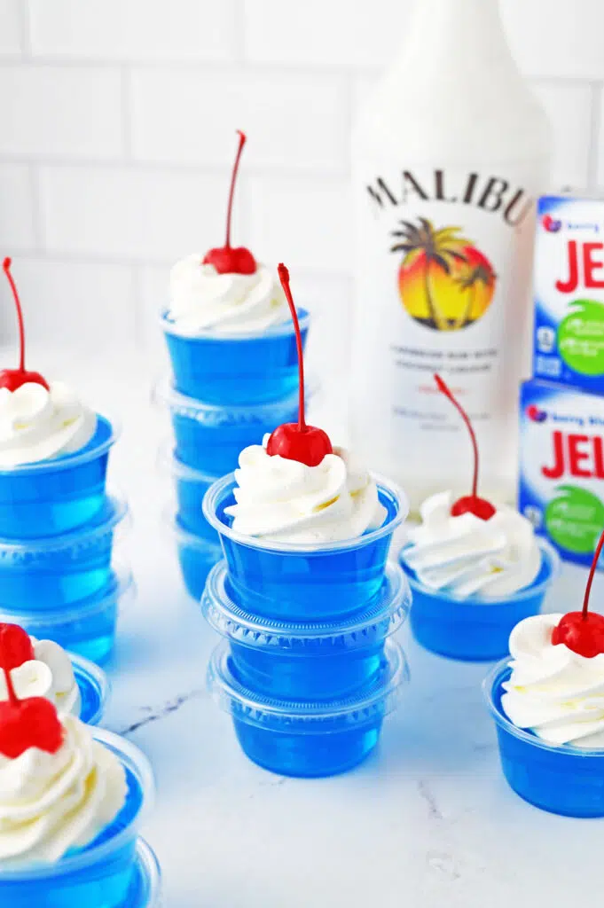 blue jello shots stacked and topped with whipped cream and maraschino cherries