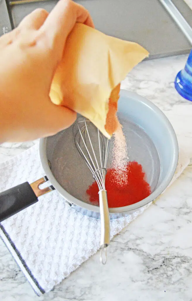 pouring red jello mix into a pot