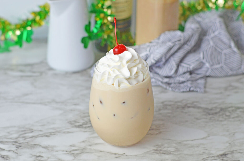 A coffee cocktail topped with fluffy whipped cream and a maraschino cherry