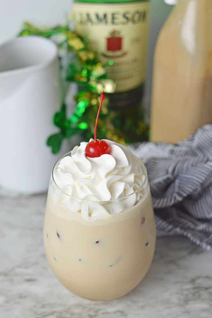 A coffee cocktail topped with fluffy whipped cream and a maraschino cherry