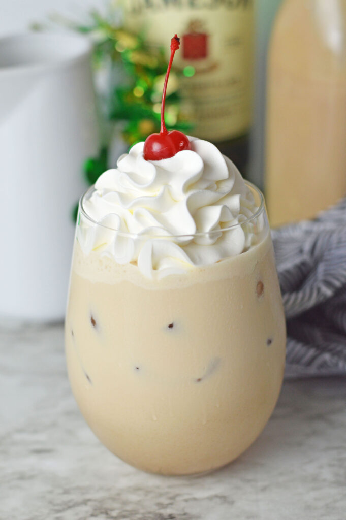 A coffee cocktail topped with fluffy whipped cream and a maraschino cherry
