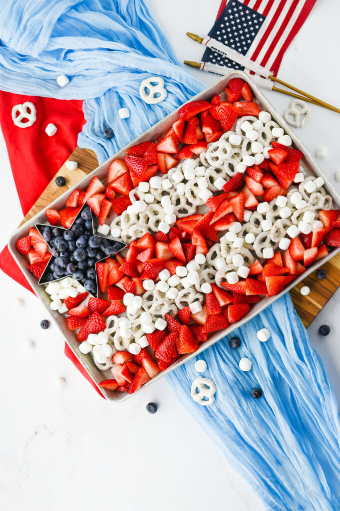 a 4th of July fruit tray with blueberries in a star shape, and stripes made from chopped strawberries and white chocolate pretzels and marshmallows