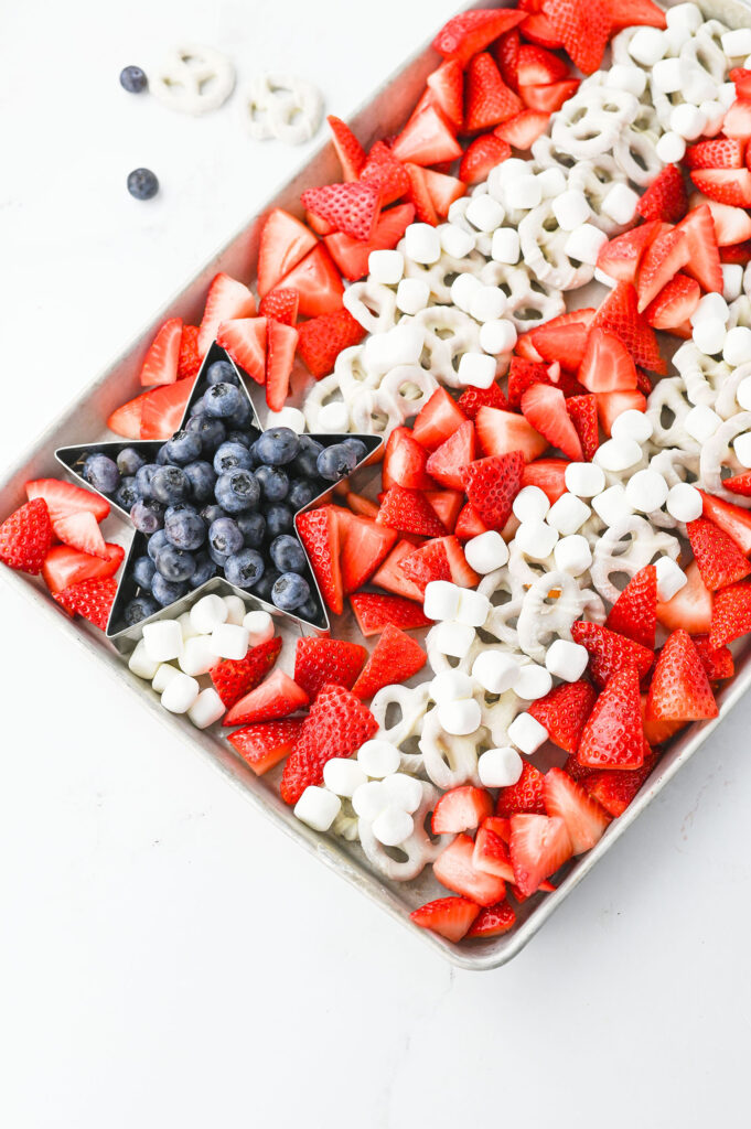 a 4th of July fruit tray with blueberries in a star shape, and stripes made from chopped strawberries and white chocolate pretzels and marshmallows