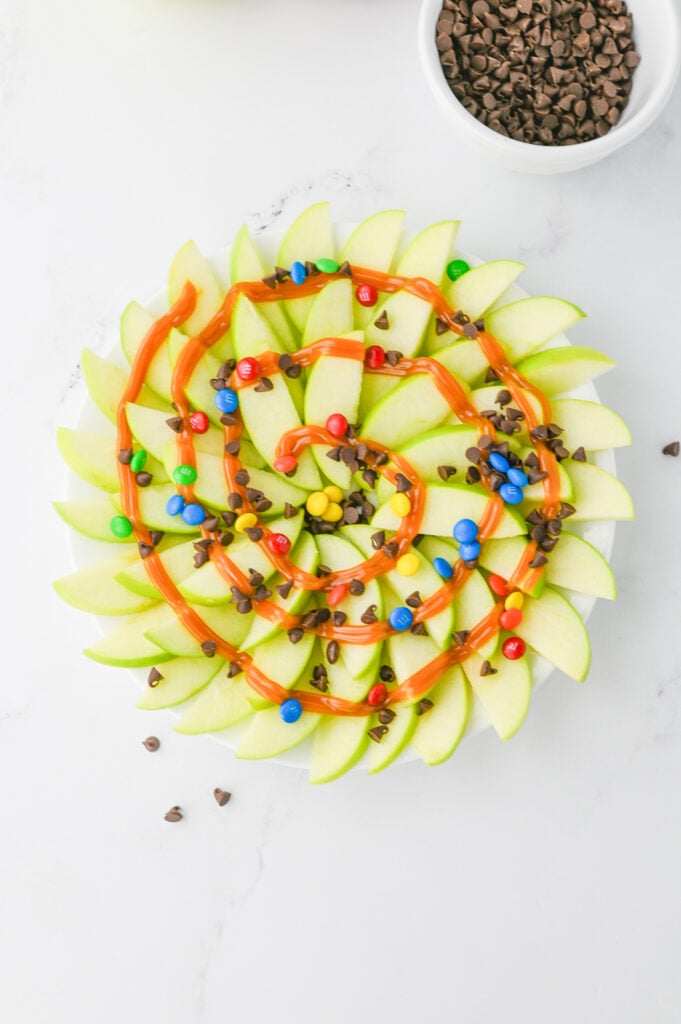 M&Ms and chocolate chips sprinkled over the caramel and apples