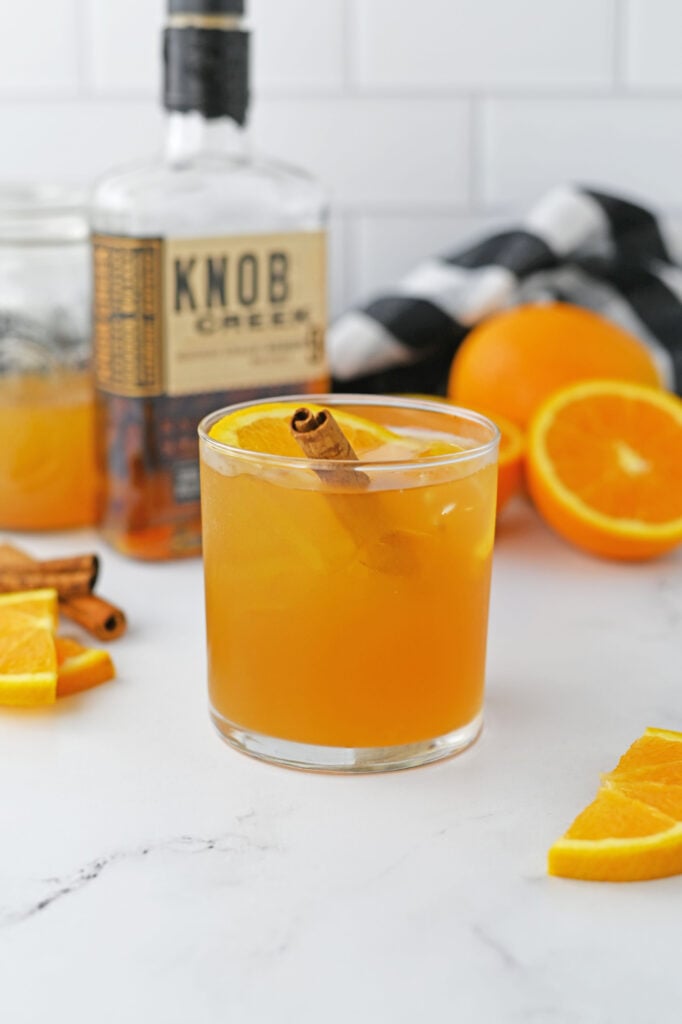 a maple cider old fashioned garnished with an orange slice and a cinnamon stick