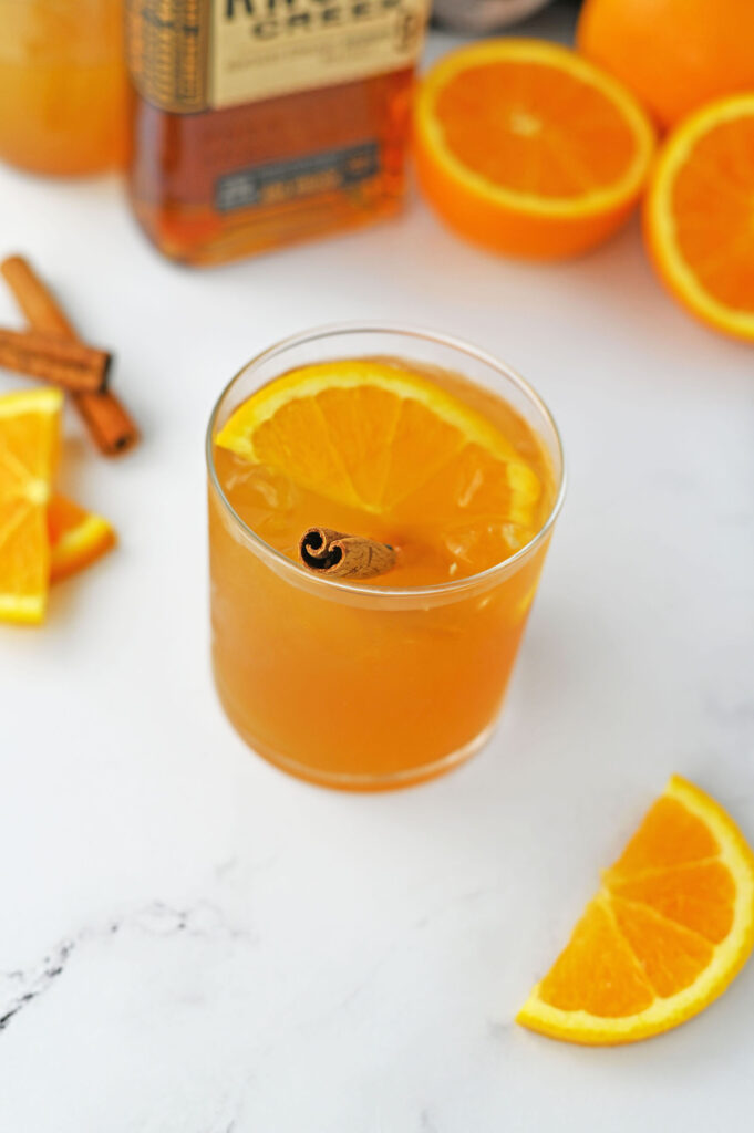 a maple cider old fashioned garnished with an orange slice and a cinnamon stick