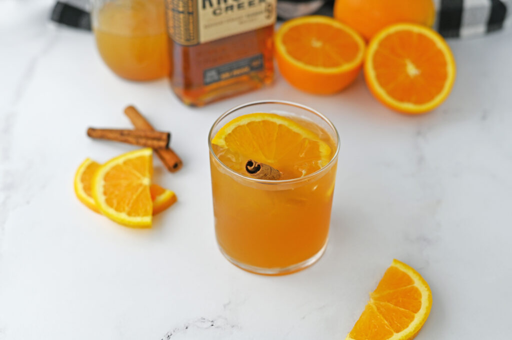 a maple cider old fashioned garnished with an orange slice and a cinnamon stick