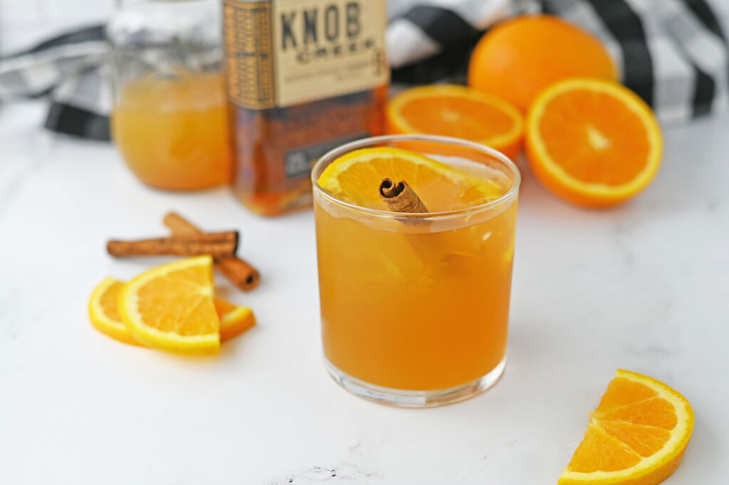 a maple cider old fashioned garnished with an orange slice and a cinnamon stick