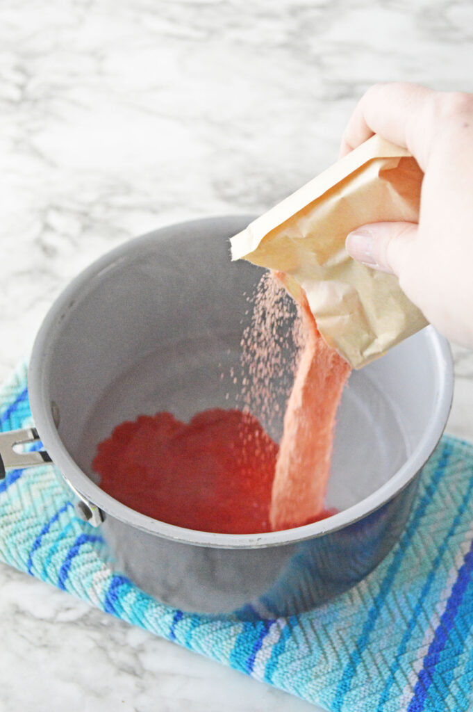 Pouring red jello into a saucepan with water.
