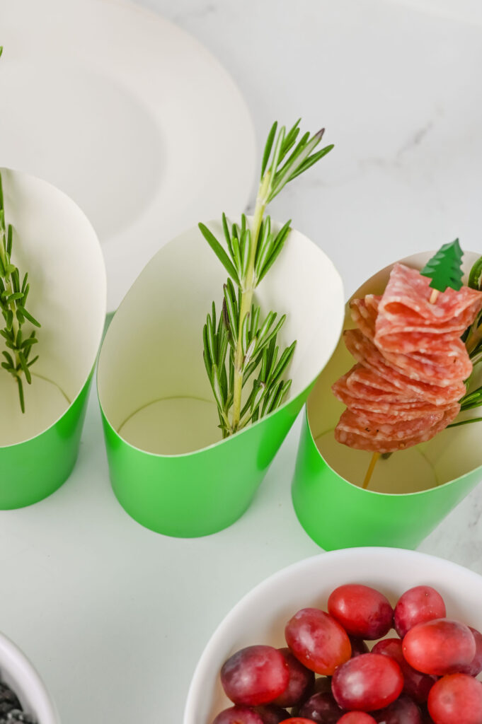 Rosemary sprigs being placed in the bottom of a charcuterie cup.