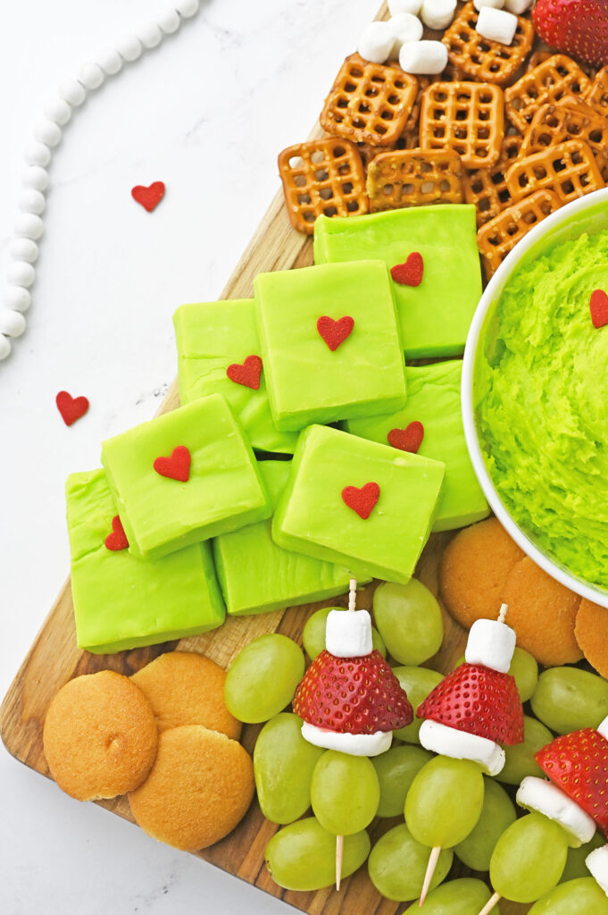 Homemade Grinch fudge squares on dessert platter surrounded by red and green treats.