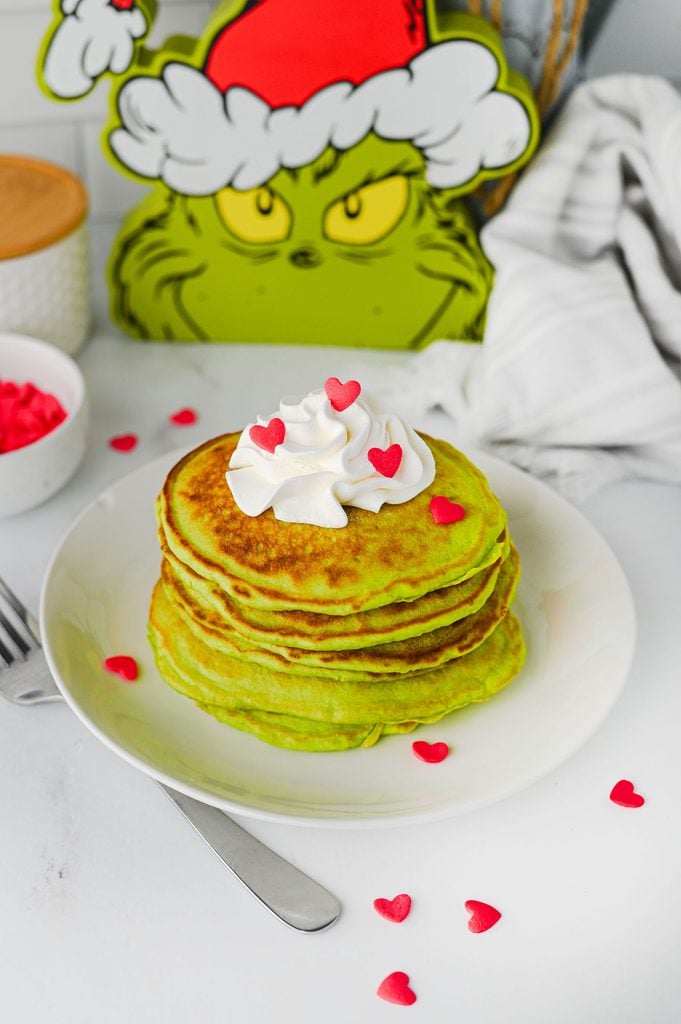 Close-up of homemade green Grinch pancakes topped with whipped cream and a red candy heart.