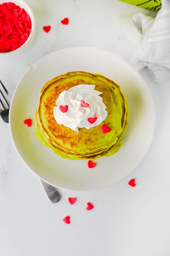 Homemade Grinch pancakes served with whipped cream and a candy heart for a festive Christmas breakfast.