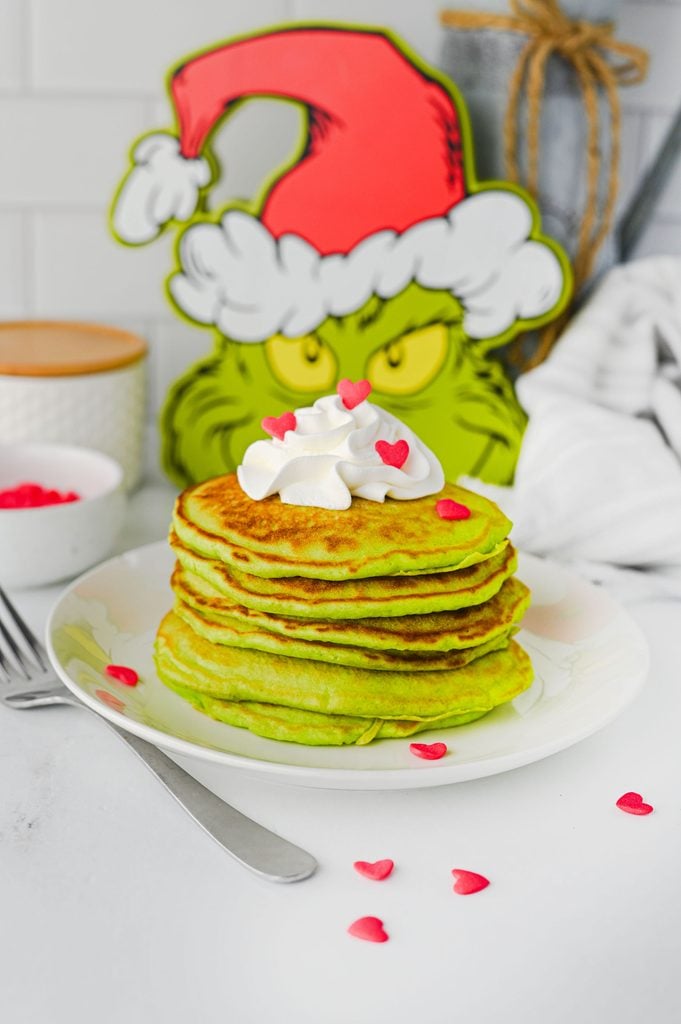 Bright green Christmas pancakes stacked on a plate with whipped cream and red heart decorations.
