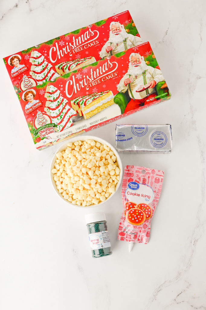 Ingredients for Christmas Tree Cake Truffles including Little Debbie snack cakes, cream cheese, white chocolate chips, red cookie icing, and green sanding sugar.