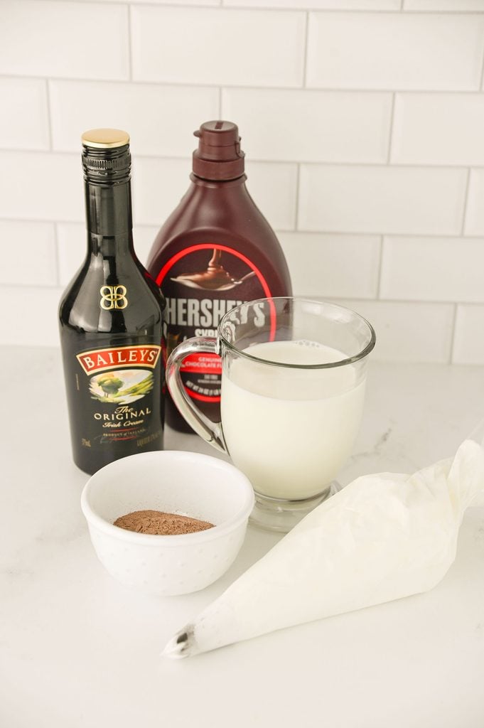 Ingredients for Baileys hot chocolate including milk, instant cocoa mix, Baileys Irish Cream, whipped cream, and chocolate sauce.