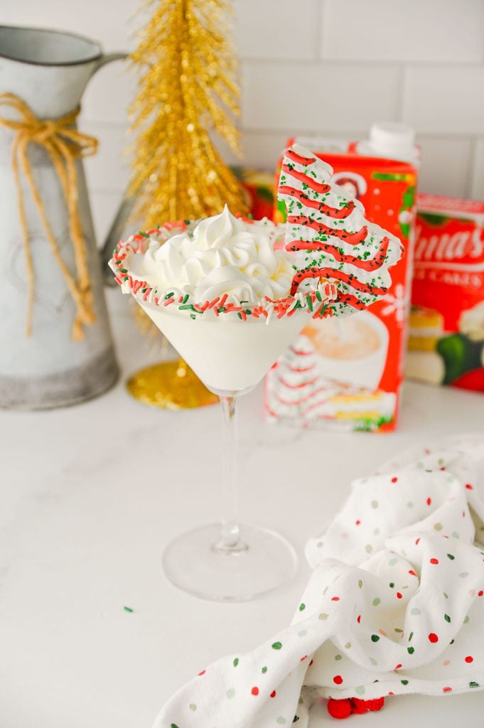 Close-up of a Christmas Tree Cake Martini with fluffy whipped cream and colorful Christmas sprinkles.