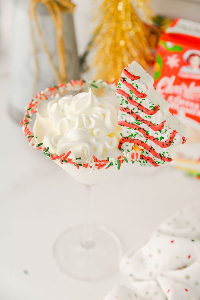 Festive Christmas Tree Cake Martini with a red and green sprinkle rim and whipped cream topping.