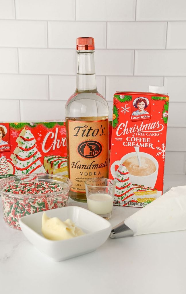 Ingredients for a Christmas Tree Cake Martini including vodka, Little Debbie Christmas Tree Cakes coffee creamer, heavy cream, frosting, sprinkles, and whipped cream.