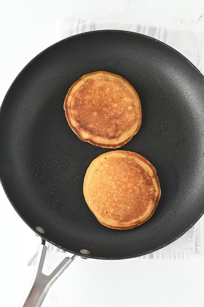 Gingerbread pancakes flipped in a skillet and cooking until golden brown.