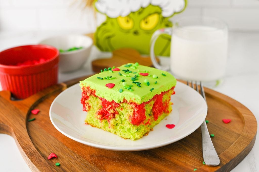 Slice of Grinch Poke Cake showing bright green cake and pockets of red cheesecake pudding filling.