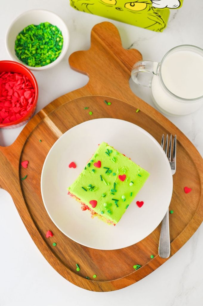 Close-up of Grinch Poke Cake decorated with green Christmas sprinkles and large red candy hearts.