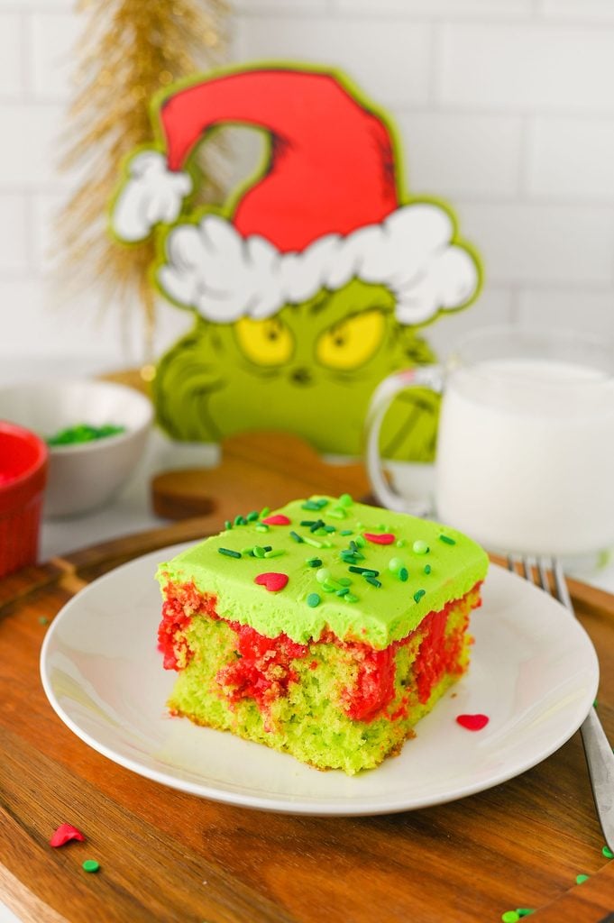 Grinch Poke Cake topped with bright green buttercream frosting, green sprinkles, and jumbo red heart sprinkles.