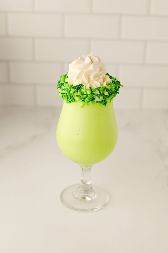 Green milkshake with whipped cream and a cherry in a sprinkle-rimmed glass