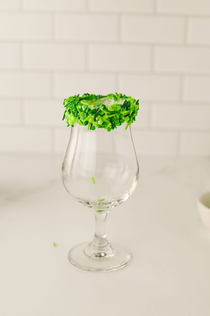 Milkshake glass rim being dipped into green sprinkles