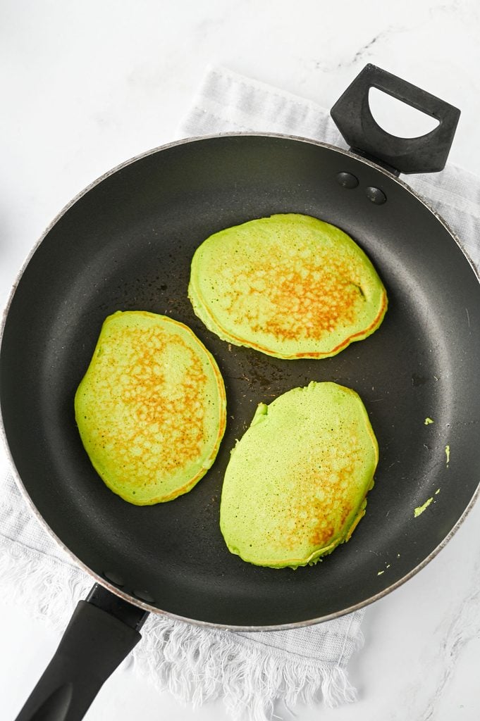 Homemade Grinch pancakes flipped in a skillet and cooking until done.