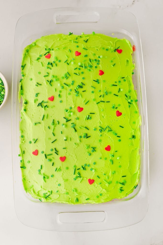 Green sprinkles and jumbo red heart sprinkles decorating a homemade Grinch Christmas cake.