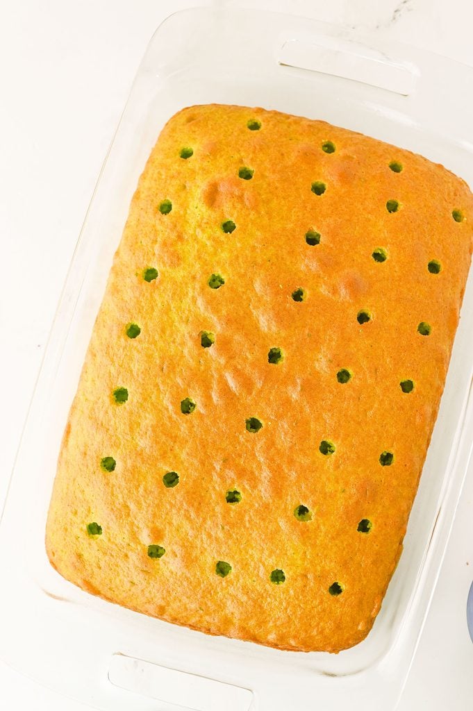 Baked green Christmas cake with holes poked throughout for cheesecake pudding filling.