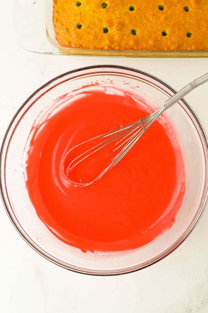 Red cheesecake instant pudding being prepared for the filling of Grinch Poke Cake.