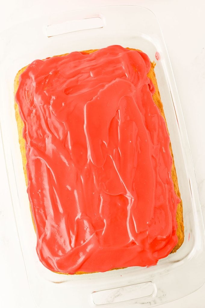 Red cheesecake pudding being added to holes in a green poke cake.
