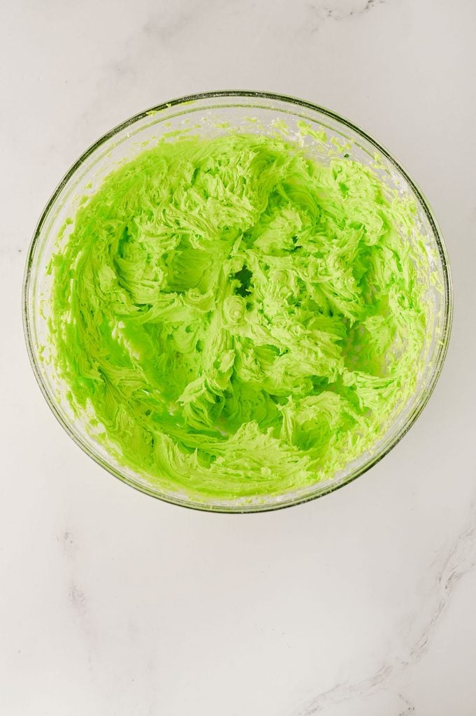 Homemade green buttercream frosting being spread over a chilled Grinch Poke Cake.