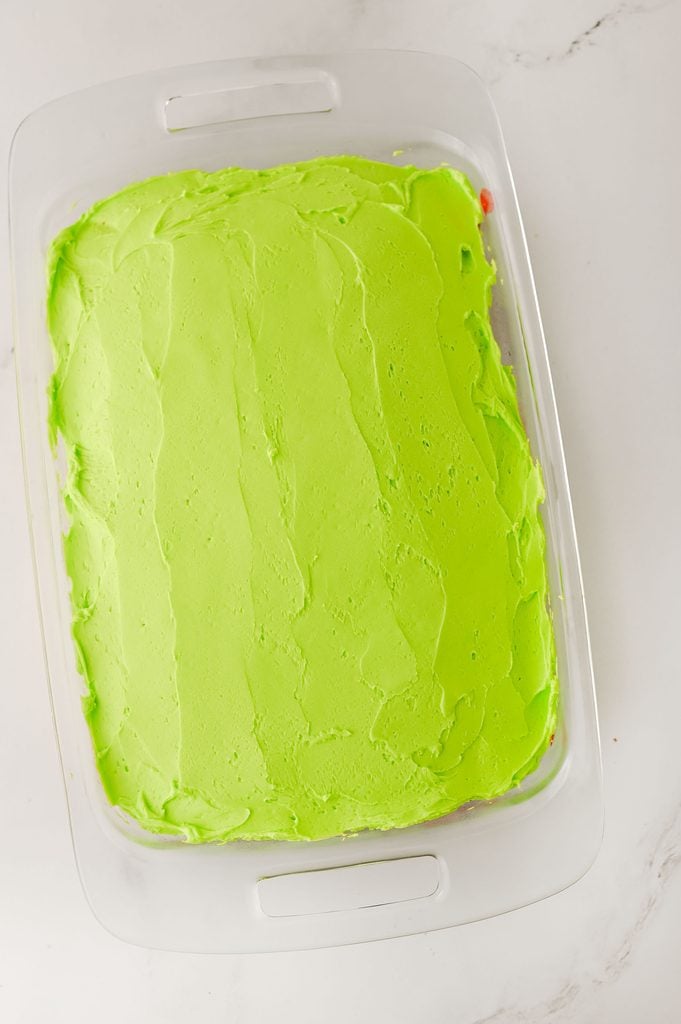 Green frosting spread over the poke cake.