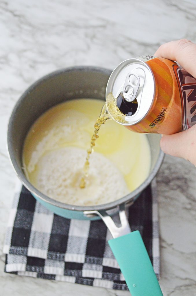 Cream soda being poured into a saucepan with the warm butterscotch mixture to make Harry Potter-inspired hot butterbeer.