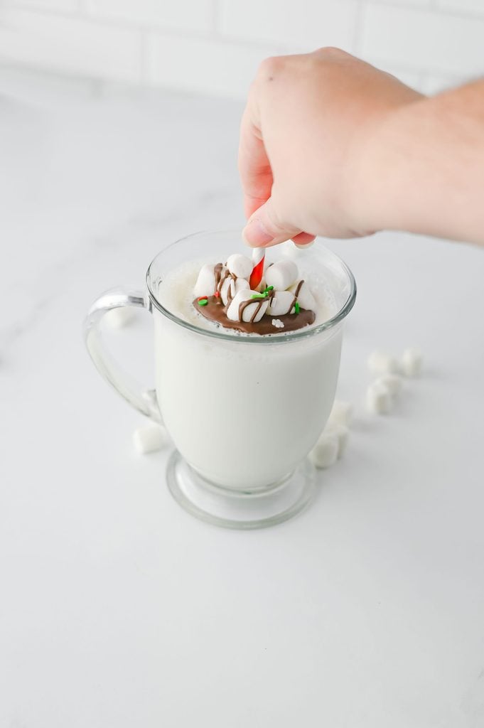 Chocolate stick melting into warm milk to make a rich cup of homemade hot chocolate