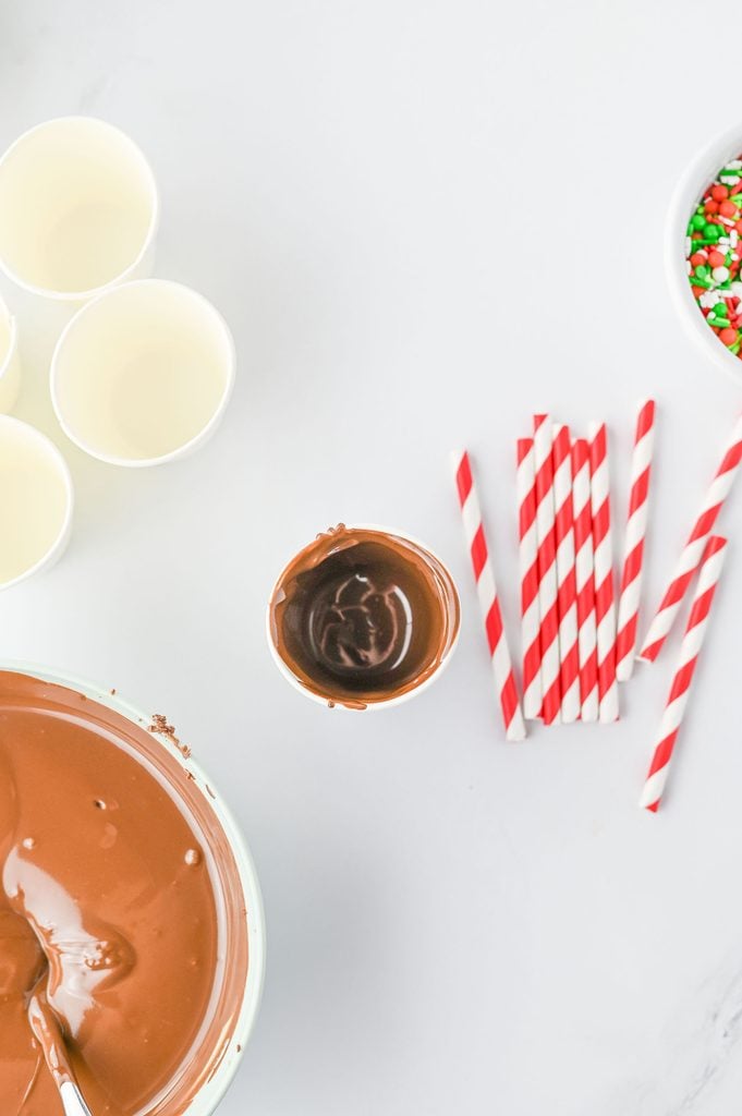 Melted chocolate poured into small paper cups to make hot chocolate on a stick