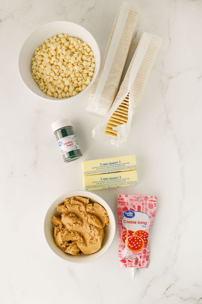 Ingredients for Christmas Tree Cake Crack including saltine crackers, butter, brown sugar, white chocolate chips, red cookie icing, and green sanding sugar.