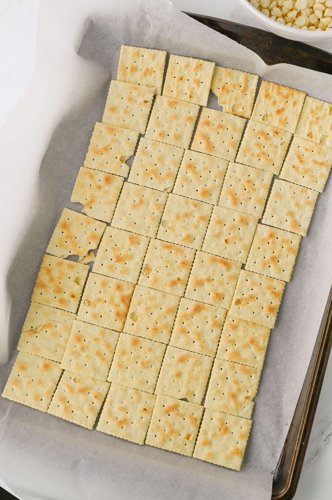 Saltine crackers arranged in a single layer on a parchment-lined baking sheet.