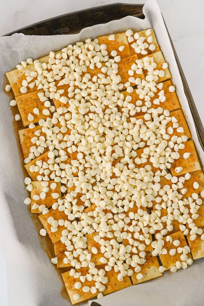 White chocolate chips sprinkled over freshly baked saltine cracker toffee.