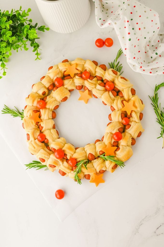 Christmas pigs in a blanket wreath decorated with cheddar cheese stars, cherry tomatoes, and fresh rosemary.