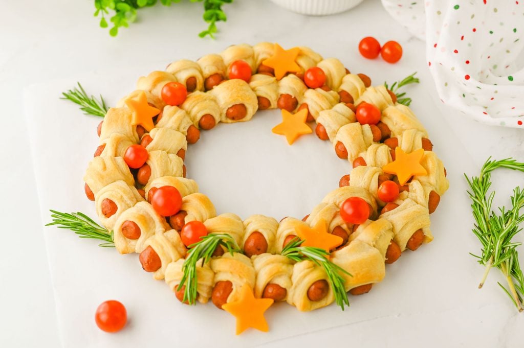 Golden baked pigs in a blanket with bright red cherry tomatoes and cheddar cheese stars for Christmas.
