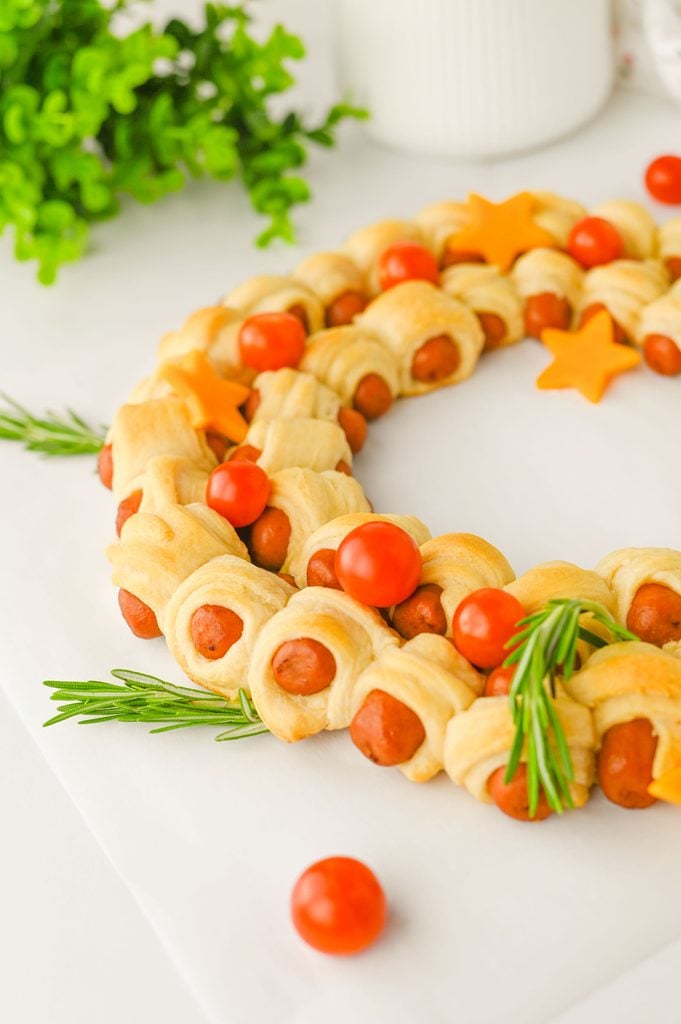 Pigs in a blanket Christmas wreath served on a white surface with fresh rosemary and festive cheese decorations.