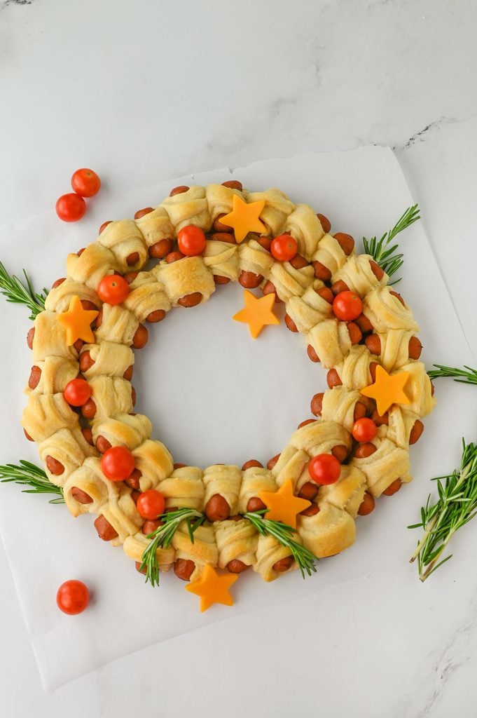 9. Adding rosemary sprigs, cheese stars, and cherry tomatoes to decorate a Christmas appetizer wreath.